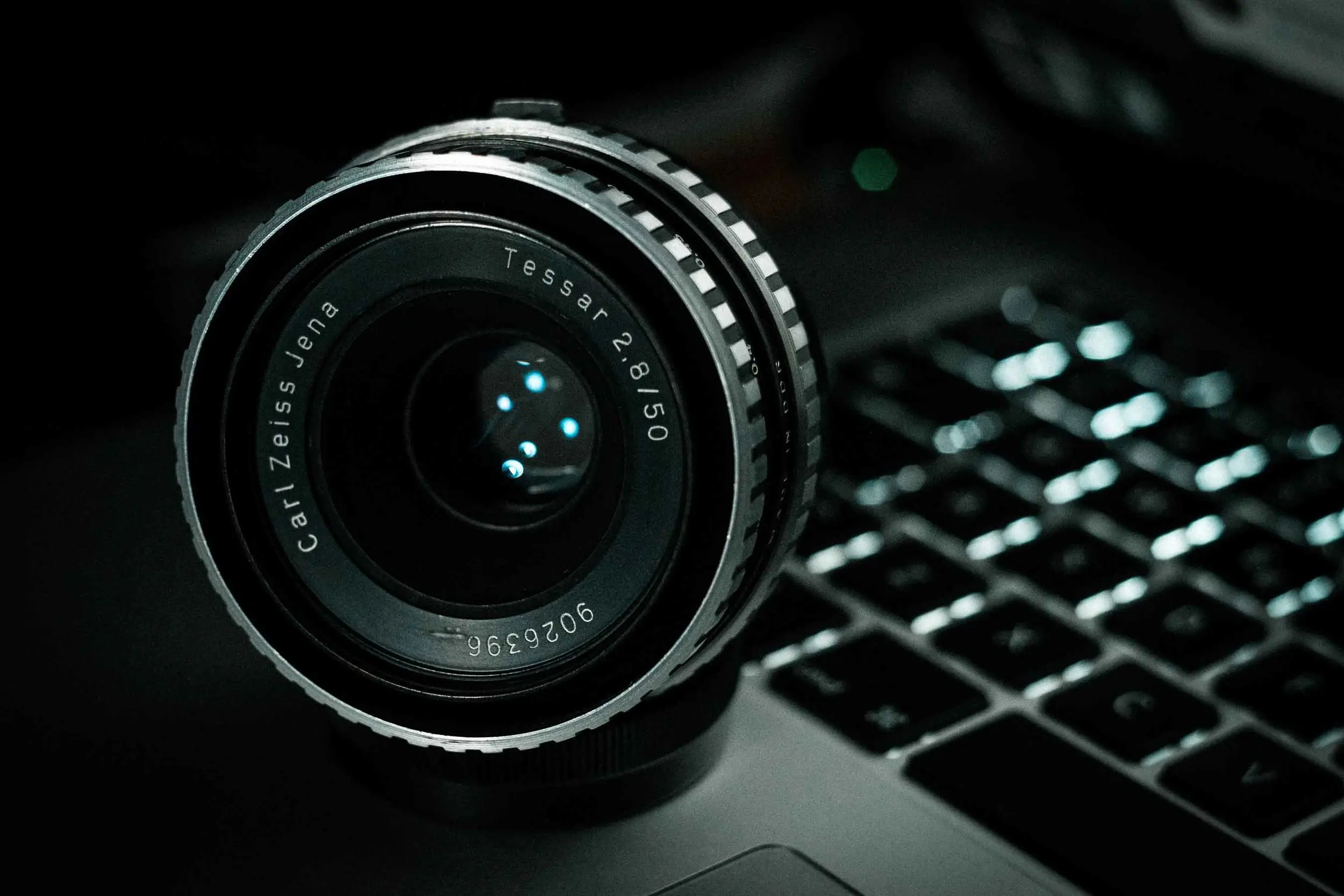 Black camera on a desk beside an open laptop in a bright room.
