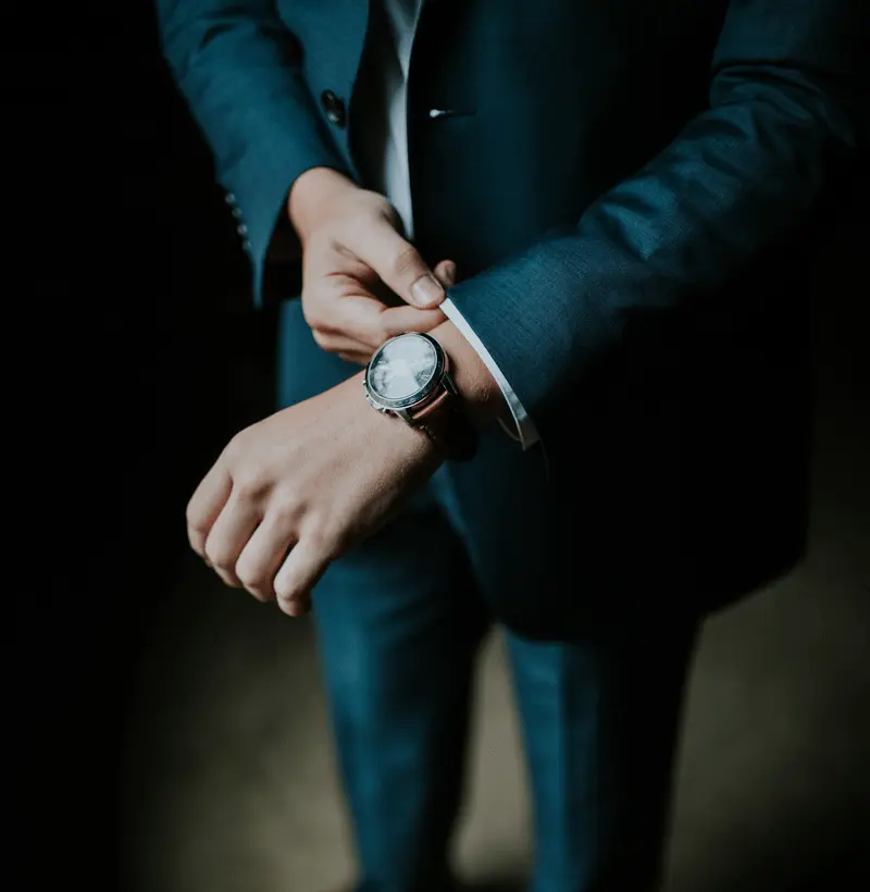 Close-up of a gray suit sleeve and a wristwatch with a brown leather strap.